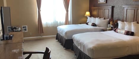 Ein Hotelzimmer mit zwei Betten, einem Schreibtisch, einem Stuhl, einer Lampe und einem gerahmten Bild an der Wand.