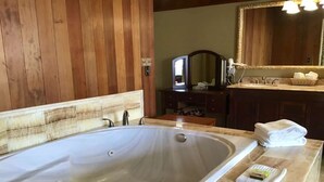 A bathroom with a large bathtub, wooden paneling, a vanity with a mirror, and a stack of towels.