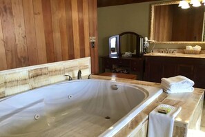 A bathroom with a large bathtub, wooden paneling, a vanity with a mirror, and a stack of towels.