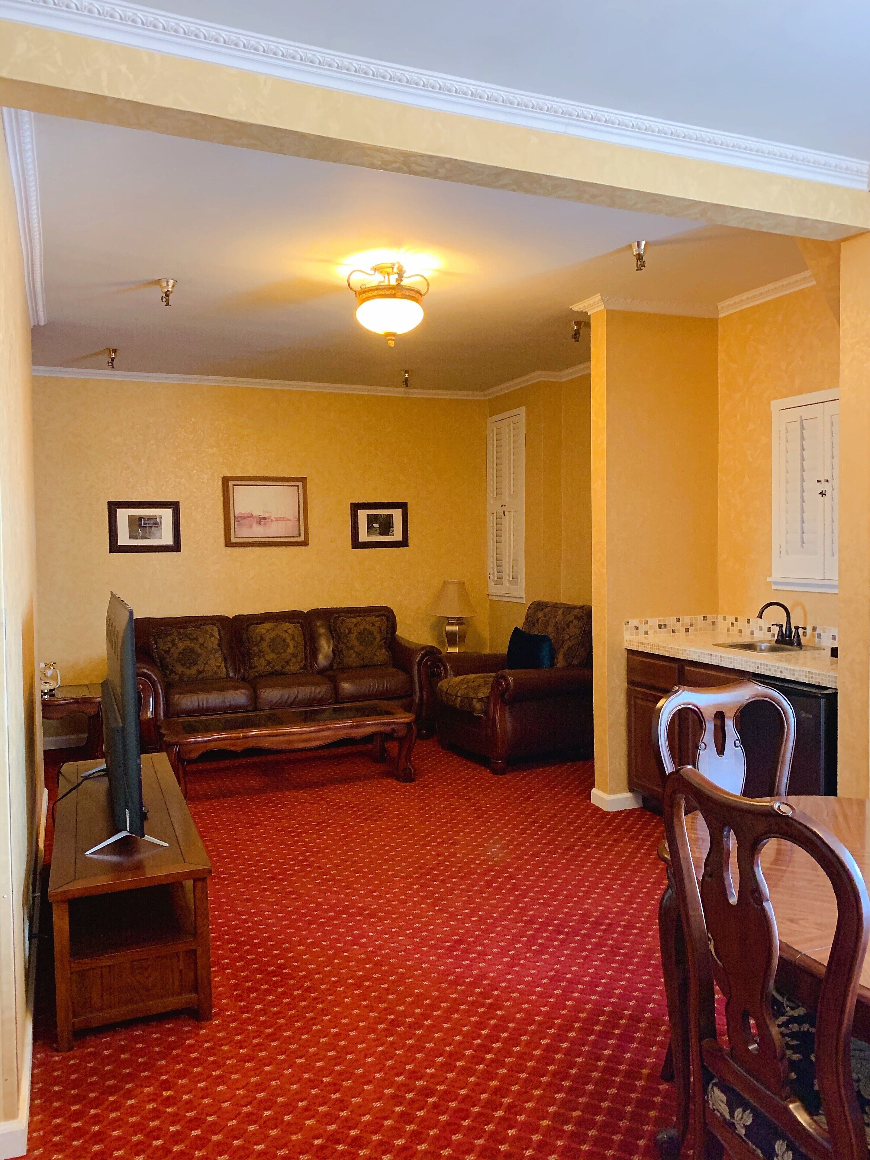 A living room with a red carpet, a sofa, a television, and a dining area with a chair and a table.