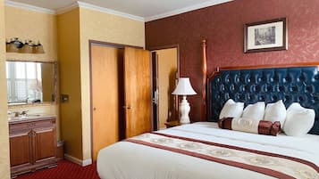 A hotel room with a large bed, a wooden wardrobe, a mirror, a bedside table with a lamp, and a framed picture on the wall.