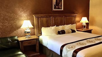 A hotel room with a wooden headboard, two bedside lamps, a black leather chair, and a bed with white bedding and decorative pillows.