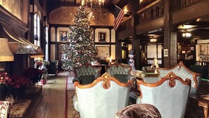 A grand hall with a large Christmas tree, elegant seating, and a high ceiling with exposed beams.