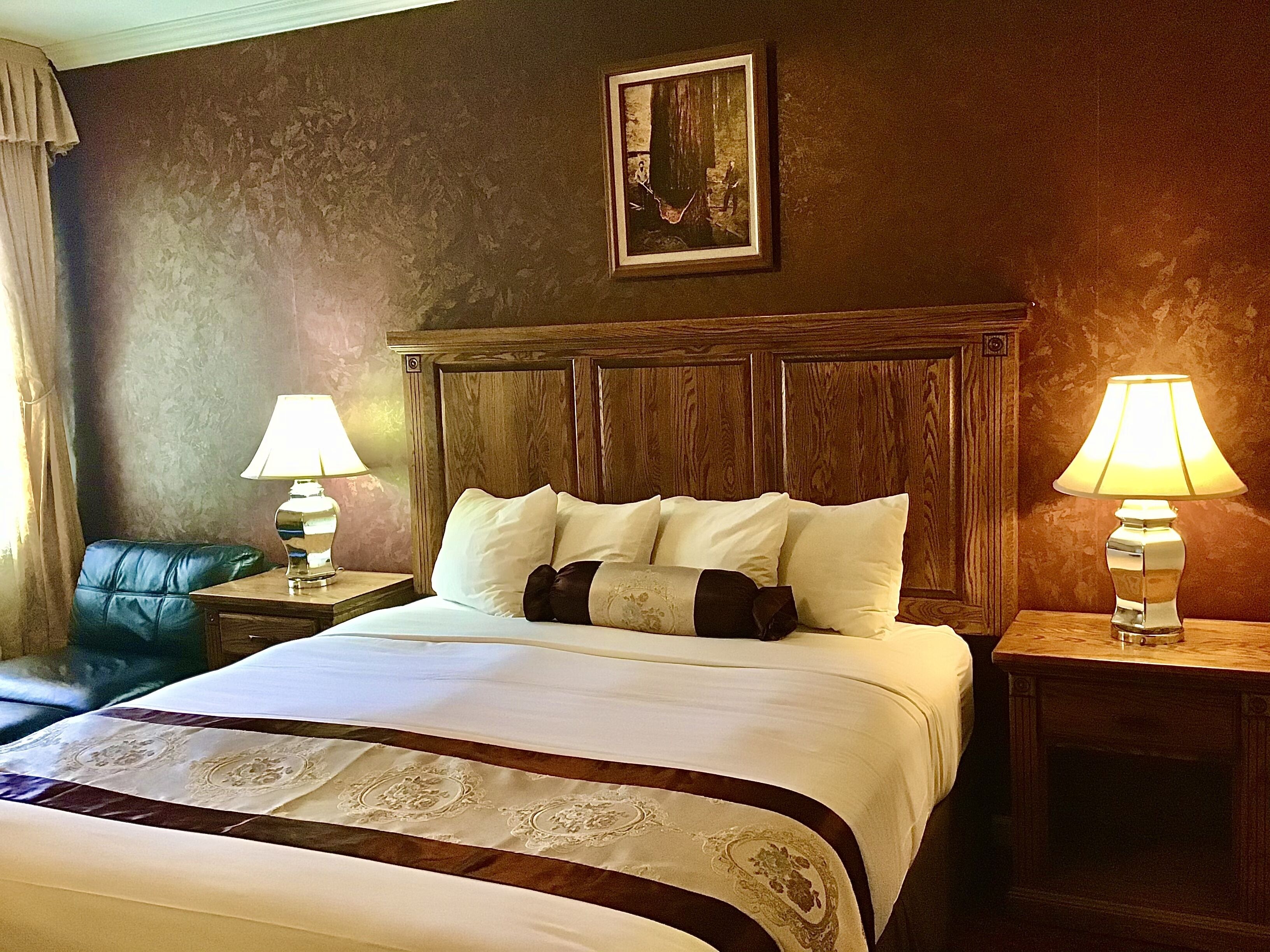 A hotel room with a large bed, two bedside tables with lamps, a headboard, and a painting on the wall.