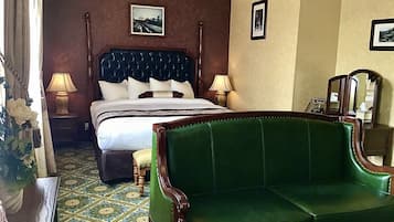 A hotel room with a large bed, two bedside lamps, a green sofa, a patterned floor, and a mirror.