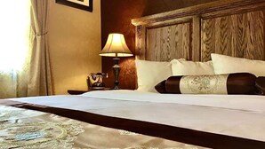 A neatly made bed with a decorative bedspread, a wooden headboard, a bedside lamp, and a telephone on a nightstand.