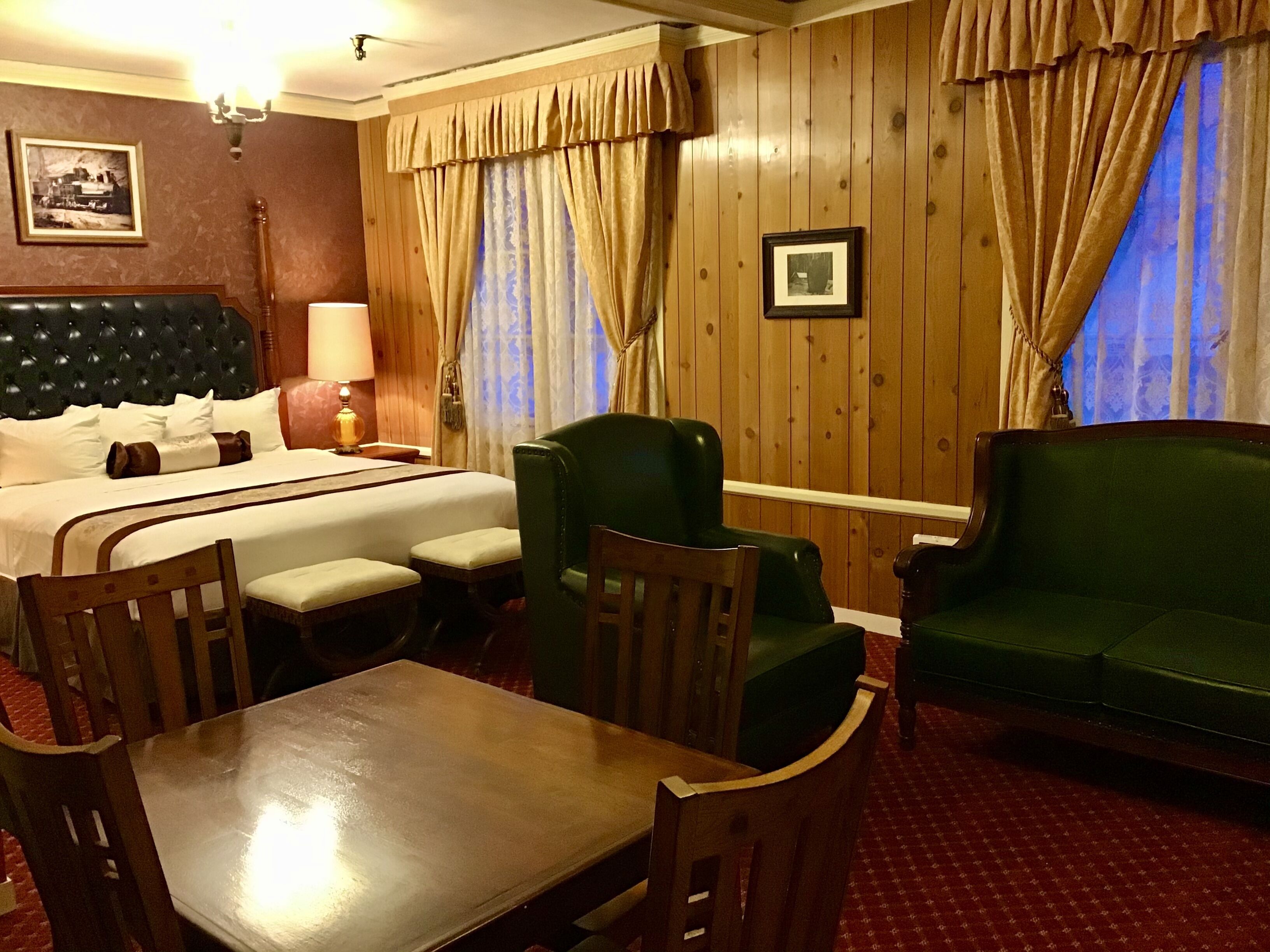 Une chambre d’hôtel avec un lit, un canapé vert, une table en bois et deux chaises.