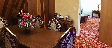 Un comedor con una mesa y sillas de madera, un jarrón de flores y una alfombra estampada.