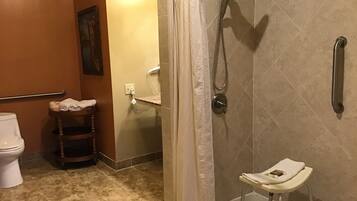 A bathroom with a shower, toilet, and a small stool.
