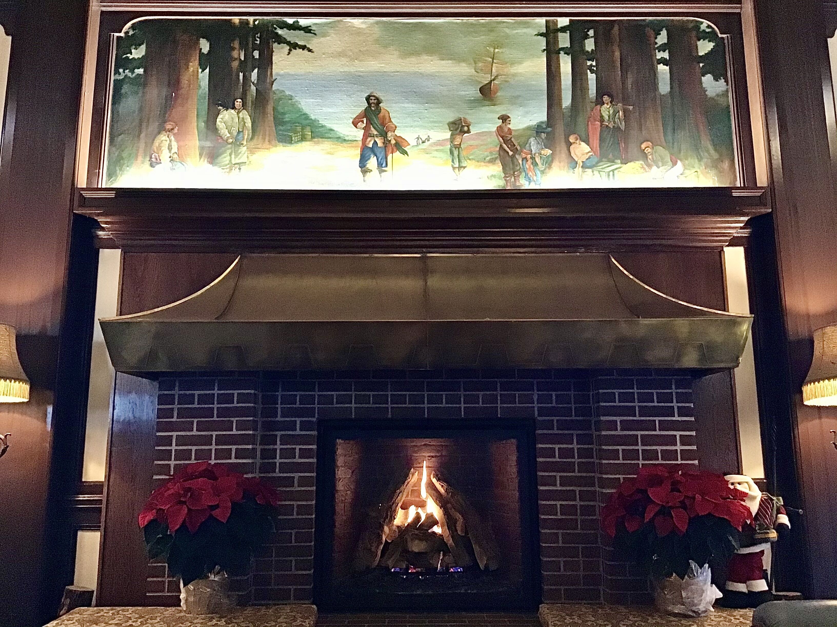 A fireplace with a painting above it, a brick wall, and two potted plants.