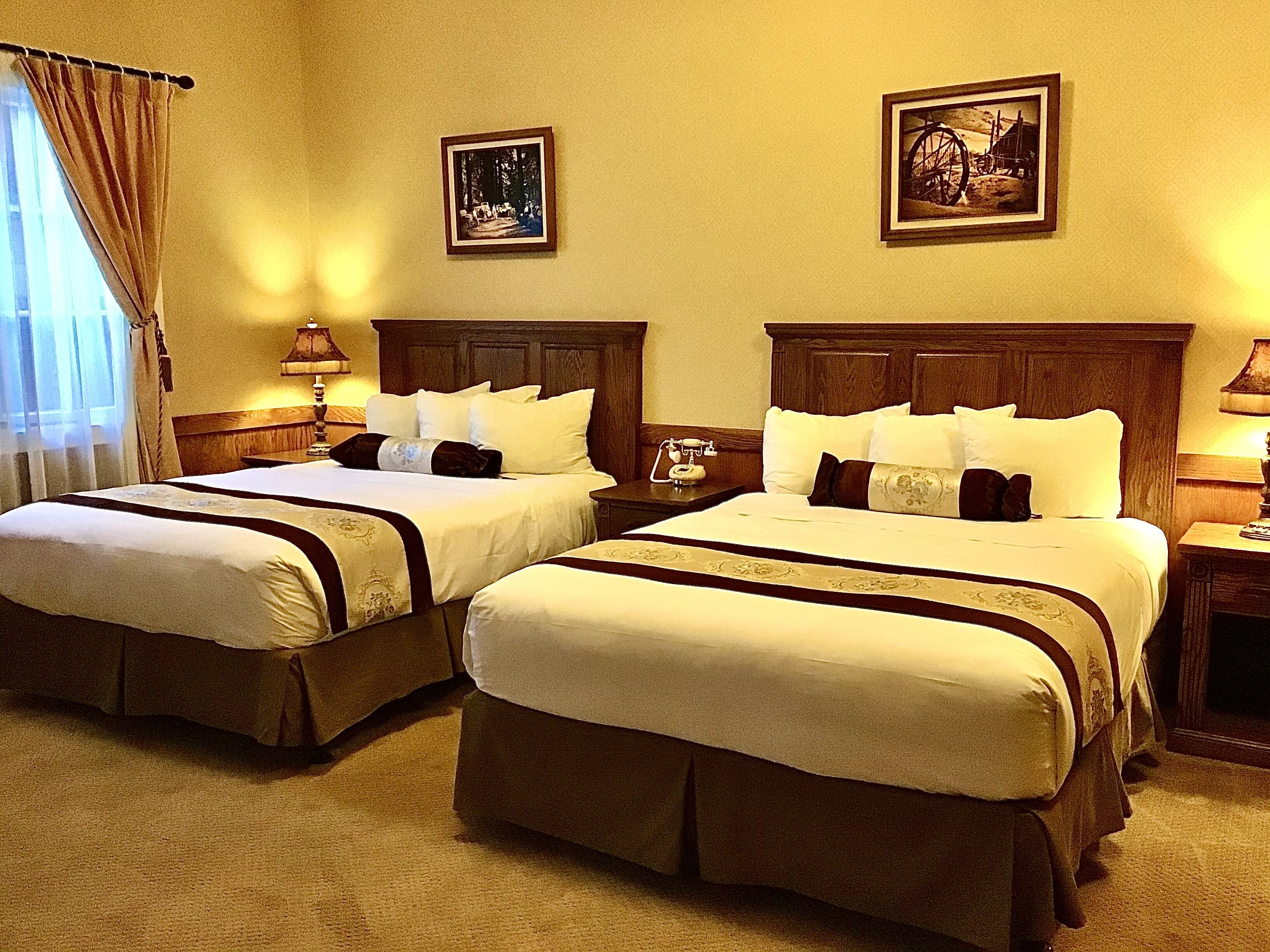 Habitación de hotel con dos camas, cada una con cabecera de madera, mesita de noche, lámpara y un cuadro en la pared.