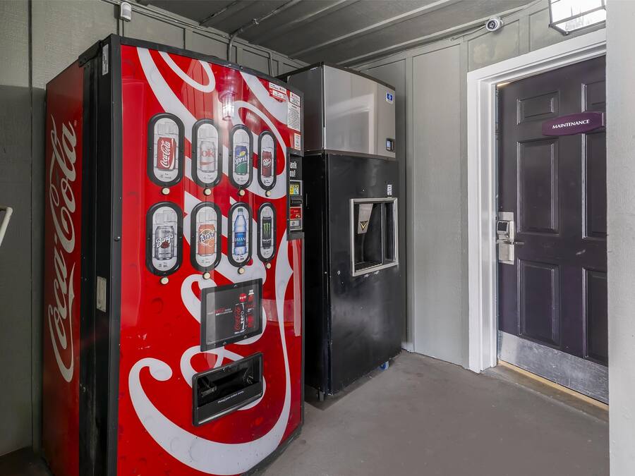 A Coca-Cola vending machine and a black refrigerator in a hallway.