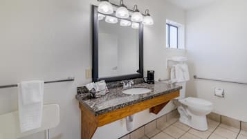 Une salle de bain avec un lavabo doté d’un plan de travail en granit, un grand miroir avec éclairage intégré, des toilettes blanches et un porte-serviettes.