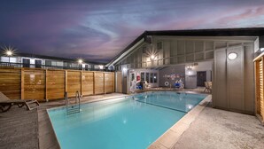 An indoor swimming pool with a wooden deck and a covered area with seating and a sauna.