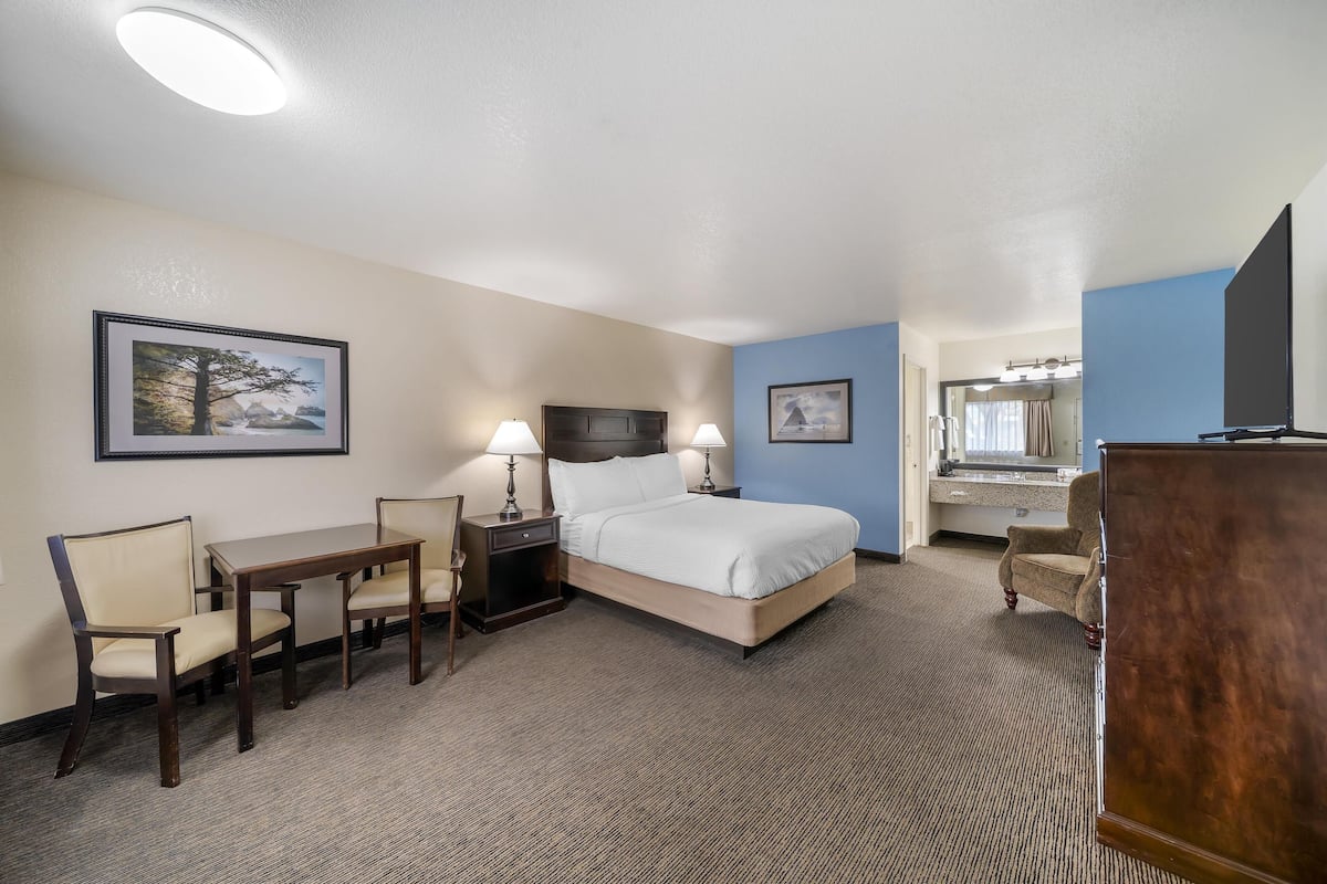 A hotel room with a bed, a desk, two chairs, a dresser, and a mirror.