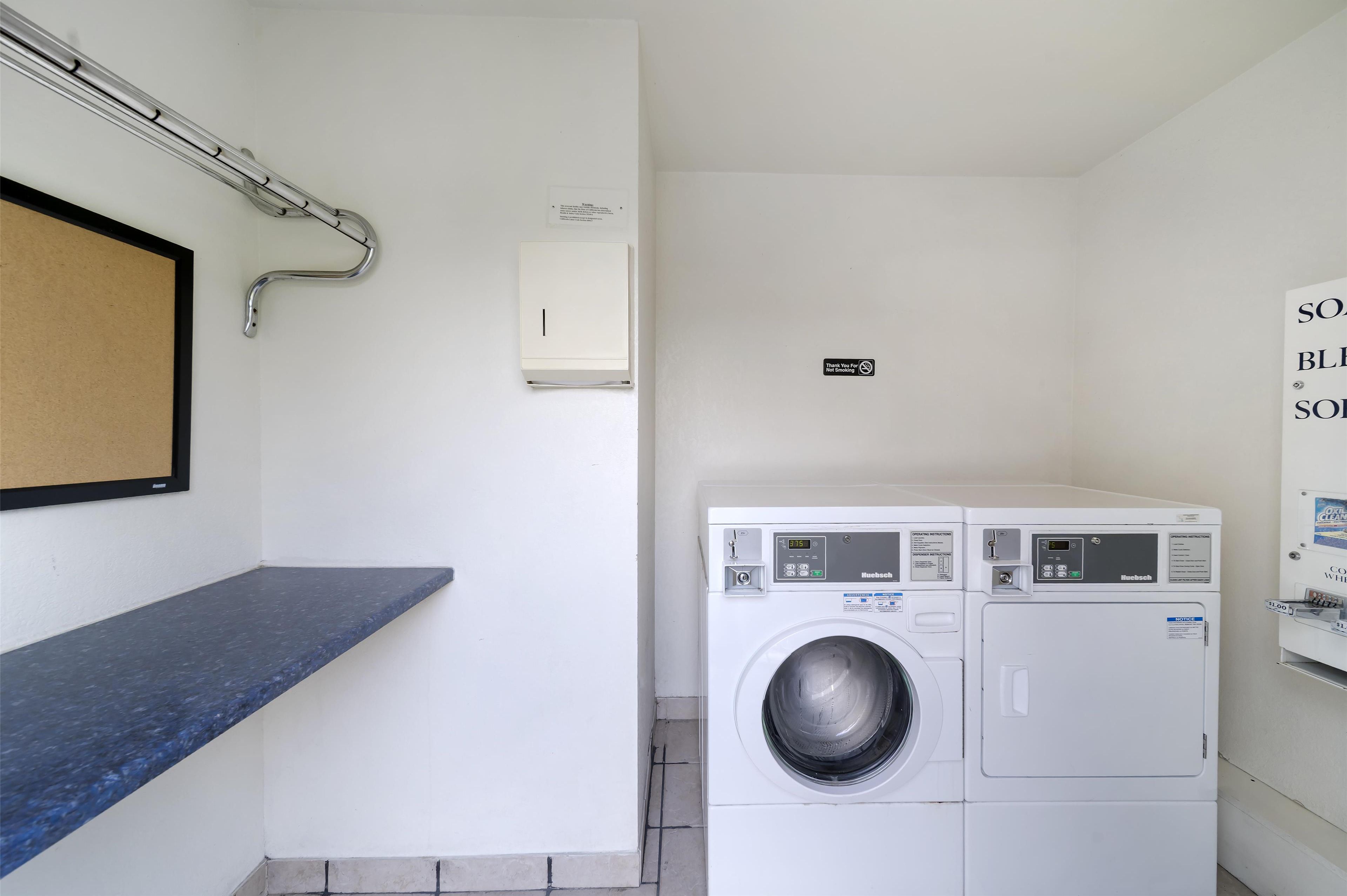 Un espace buanderie comprenant un lave-linge, un sèche-linge, un porte-serviettes et un panneau indiquant la fonction de la pièce.
