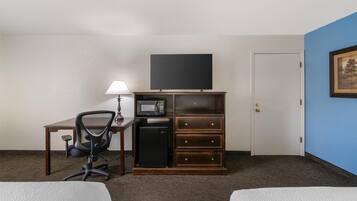 Een hotelkamer met een bed, een bureau met lamp, een televisie, een magnetron, een koelkast en een dressoir.