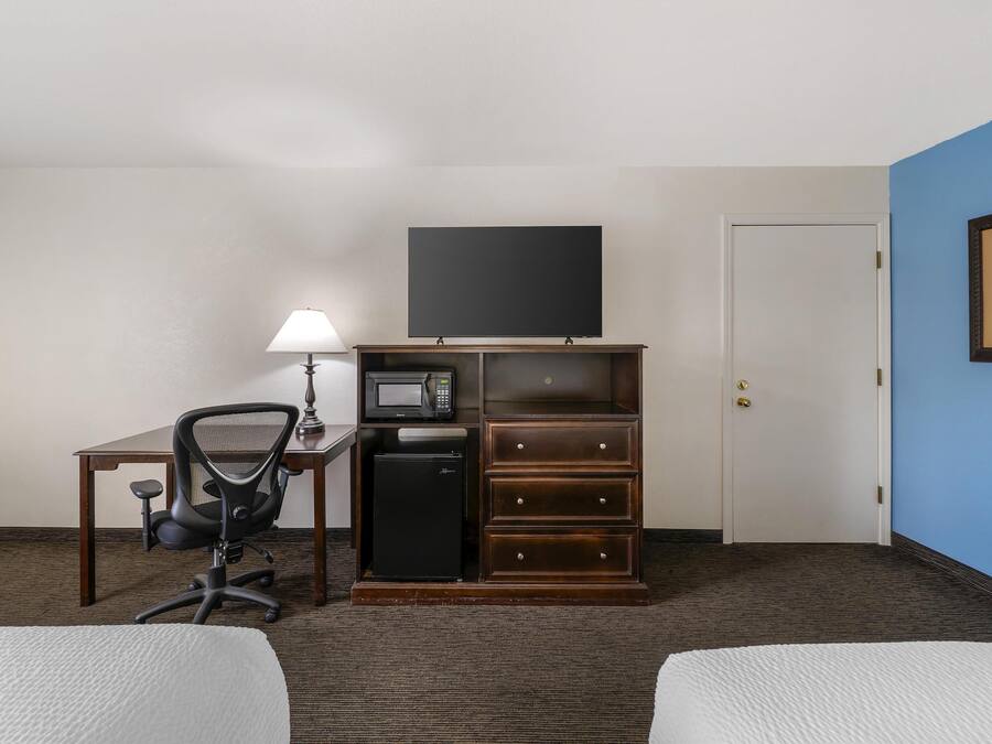 Een hotelkamer met een bed, een bureau met lamp, een televisie, een magnetron, een koelkast en een dressoir.