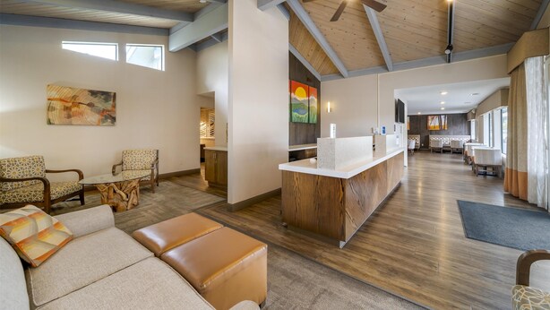 A spacious living area with a wooden ceiling, a central island with a wooden base, and a seating area with patterned chairs and a sofa.