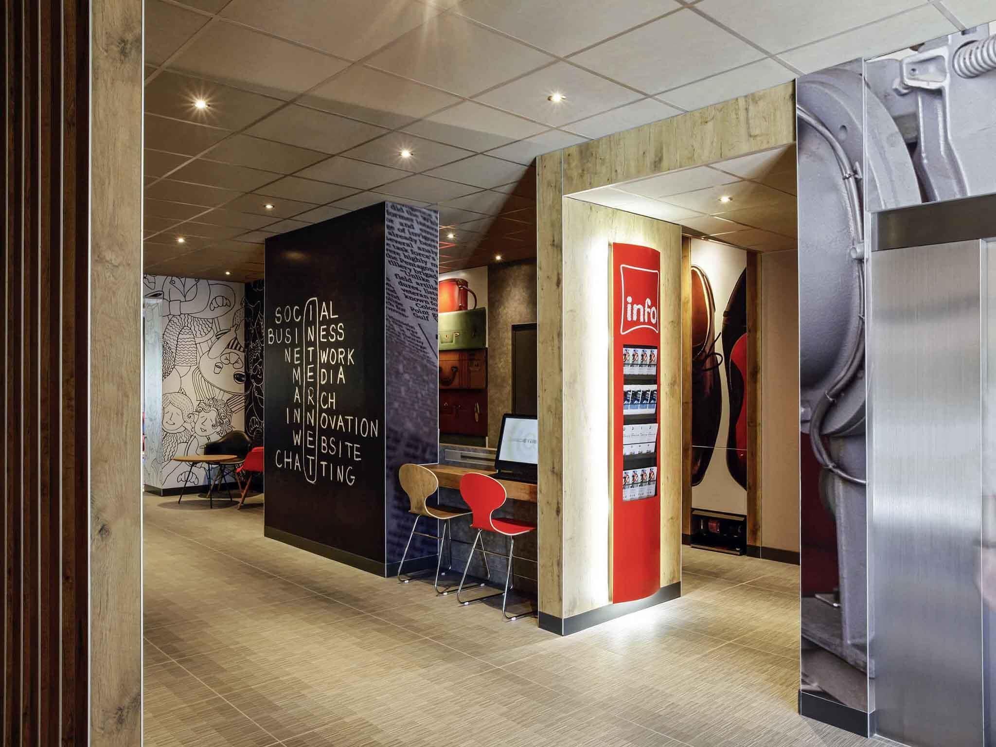 Un interior moderno con suelo de madera, un separador negro con texto blanco, sillas rojas y un expositor rojo y blanco con información.