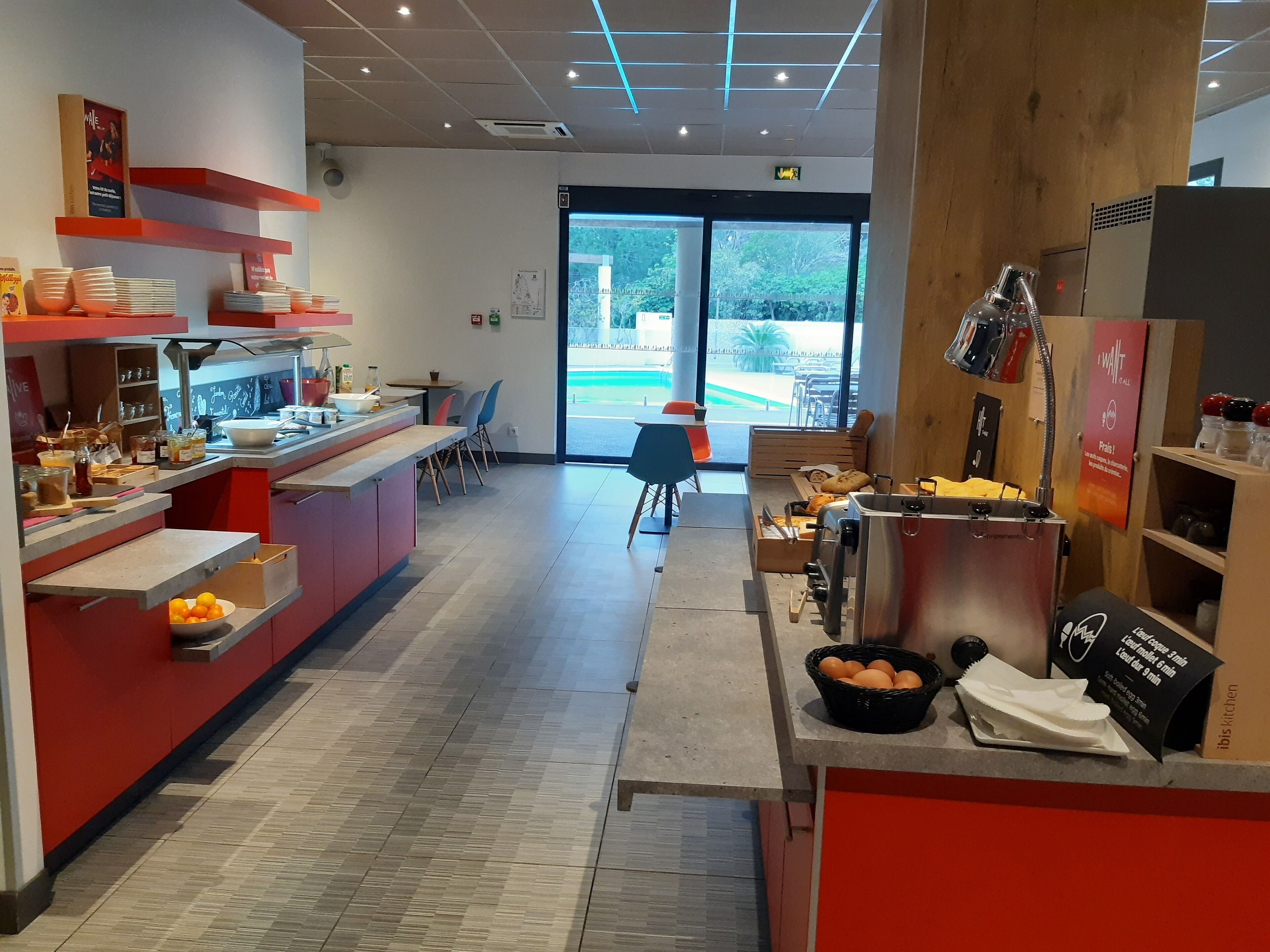 A modern kitchen area with a counter, shelves with kitchenware, and a view of the outdoors through large windows.