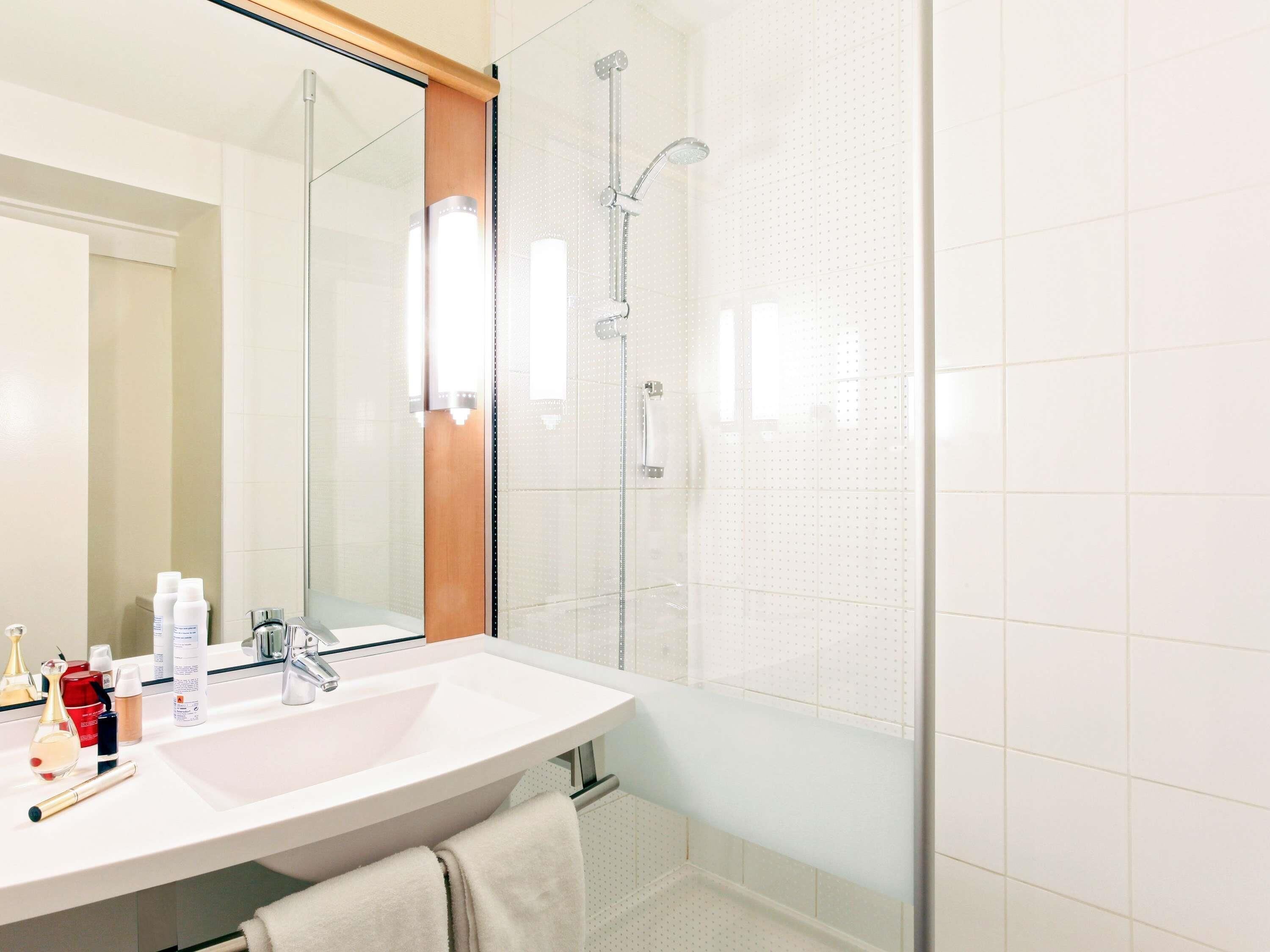 A bathroom with a white sink, a mirror, a glass shower enclosure, and toiletries on the counter.