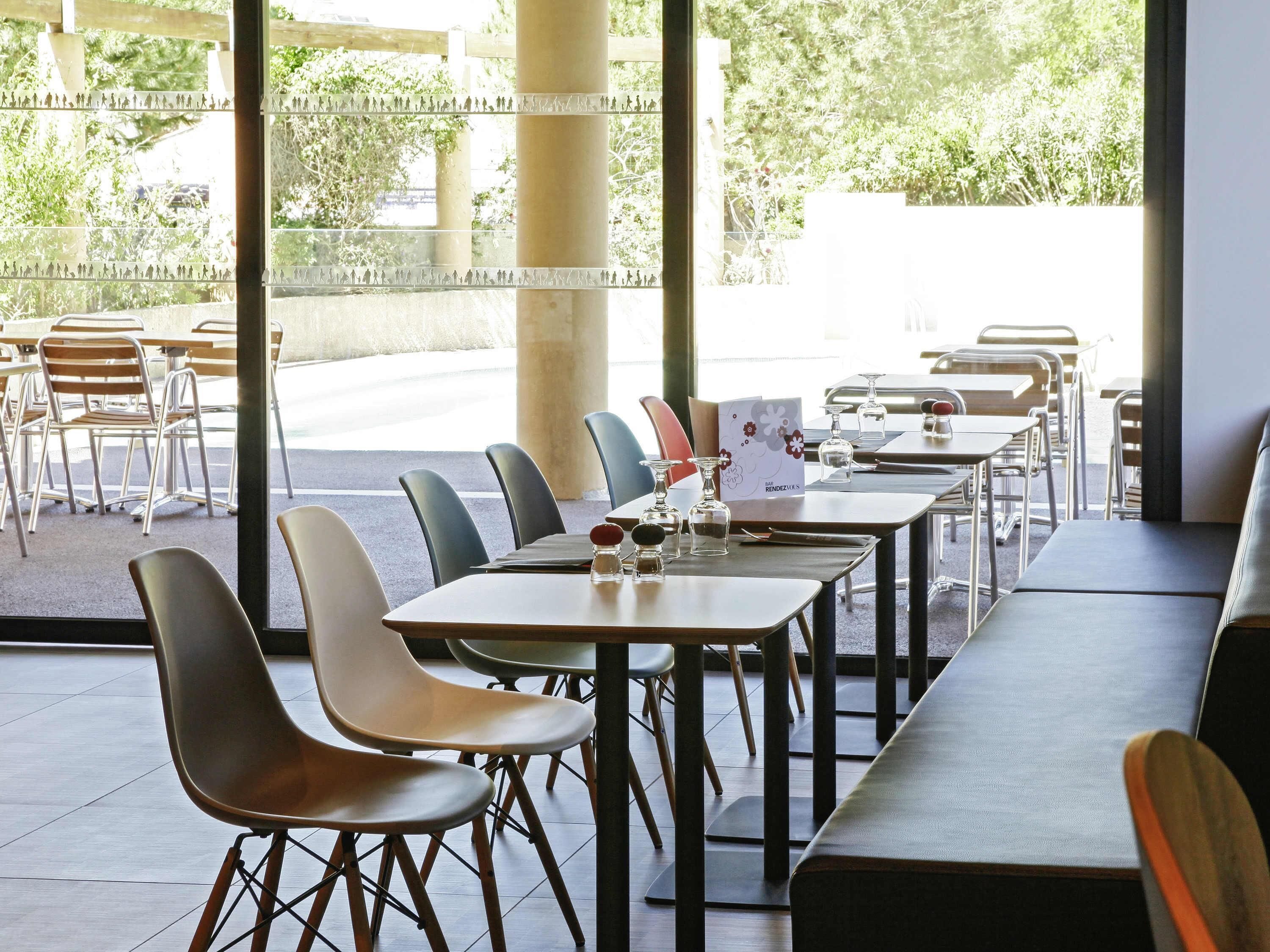 Un espace de restauration intérieur avec des tables et des chaises, de grandes fenêtres et une vue sur l’extérieur.