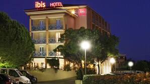 A multi-story hotel with balconies, a prominent 'ibis HOTEL' sign, and a parking area with cars. - ibis Hyères Centre (Hyères)