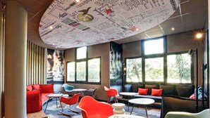 A modern lounge with red and blue seating, large windows, and a ceiling covered in handwritten notes. - ibis Hyères Centre (Hyères)