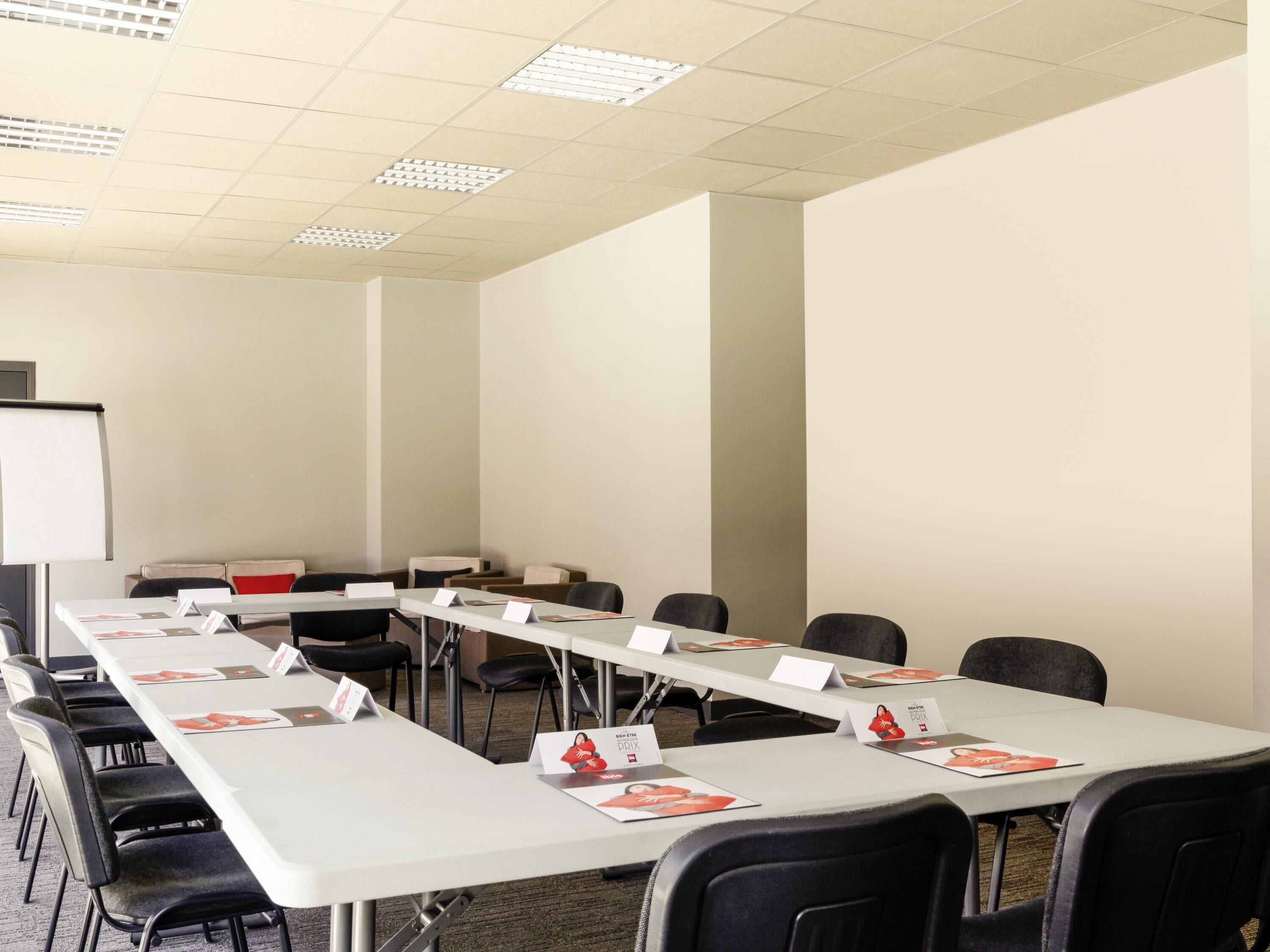 Un salón de conferencias con una larga mesa, sillas negras, tarjetas de nombres y una pizarra.