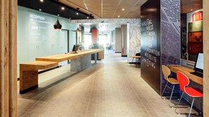 A modern reception area with a reception desk, seating, and a wall with social media and business-related graphics. - ibis Hyères Centre (Hyères)