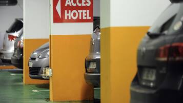 Un aparcamiento con coches estacionados en plazas delimitadas, un cartel que indica 'ACCESS HOTEL' y un suelo verde con líneas blancas para marcar los espacios.