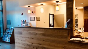 A reception desk with a wooden finish, overhead lighting, and a glass display case with pastries.