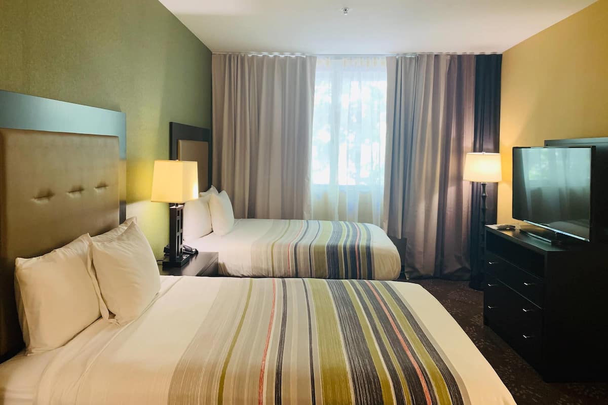 A hotel room with two beds, a TV, a desk, and a window with curtains.
