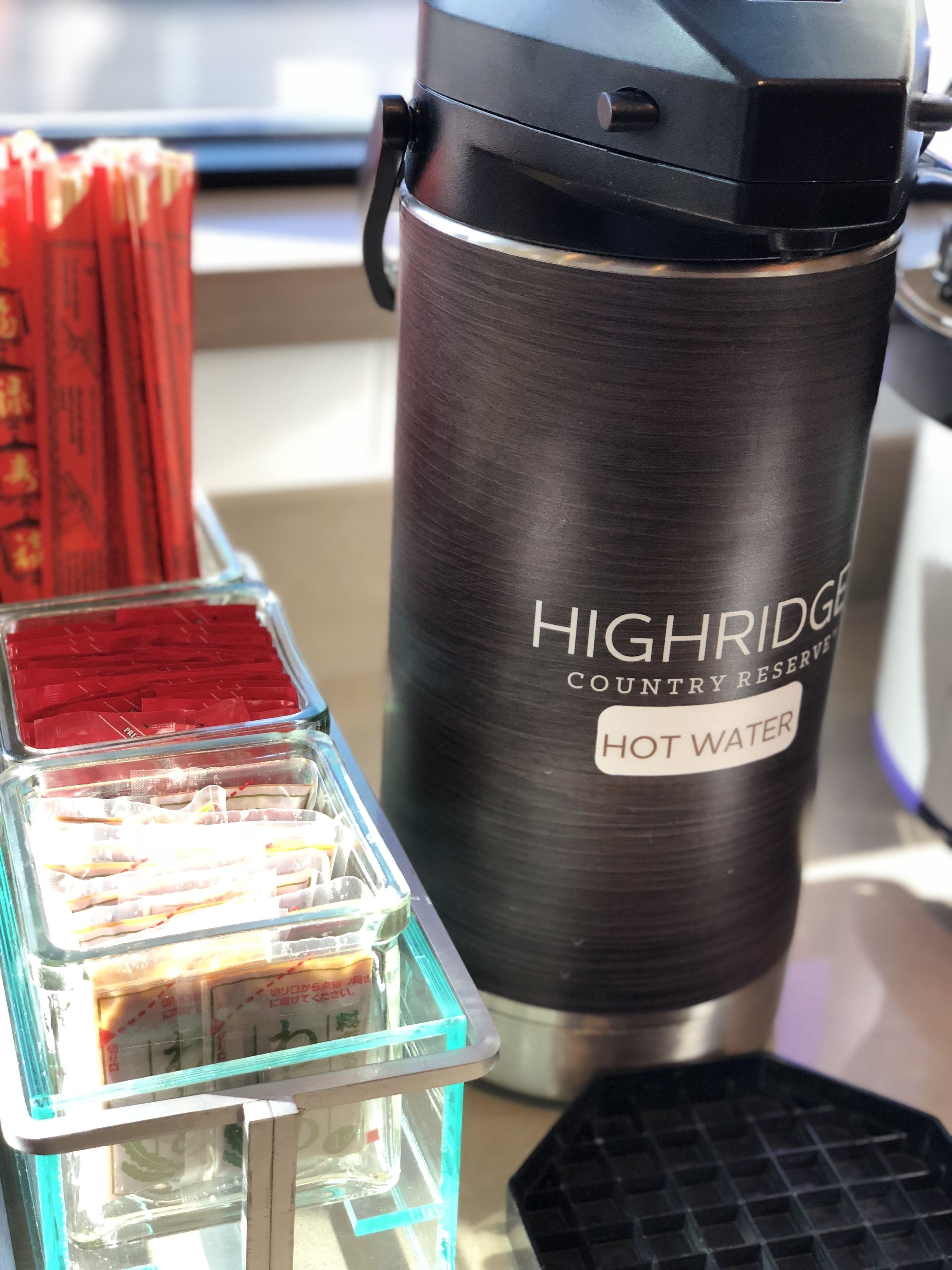 A black thermos labeled "Highridge Country Reserve Hot Water" next to a glass container with red packets.