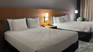 A hotel room with two beds, a wooden headboard, a nightstand with a phone, and a lamp.