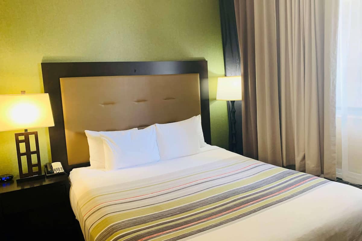 A hotel room with a large bed, two bedside lamps, a nightstand with a phone, and a window with curtains.