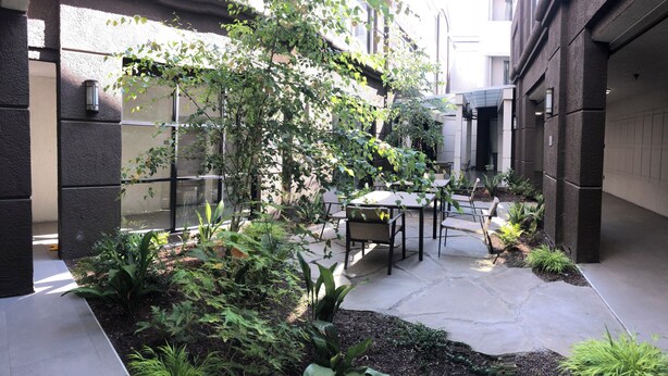 A courtyard with a table and chairs, surrounded by greenery and a glass wall.