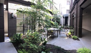 A courtyard with a table and chairs, surrounded by greenery and a glass wall. - Country Inn & Suites by Radisson, San Jose International Airport, CA (San Jose)