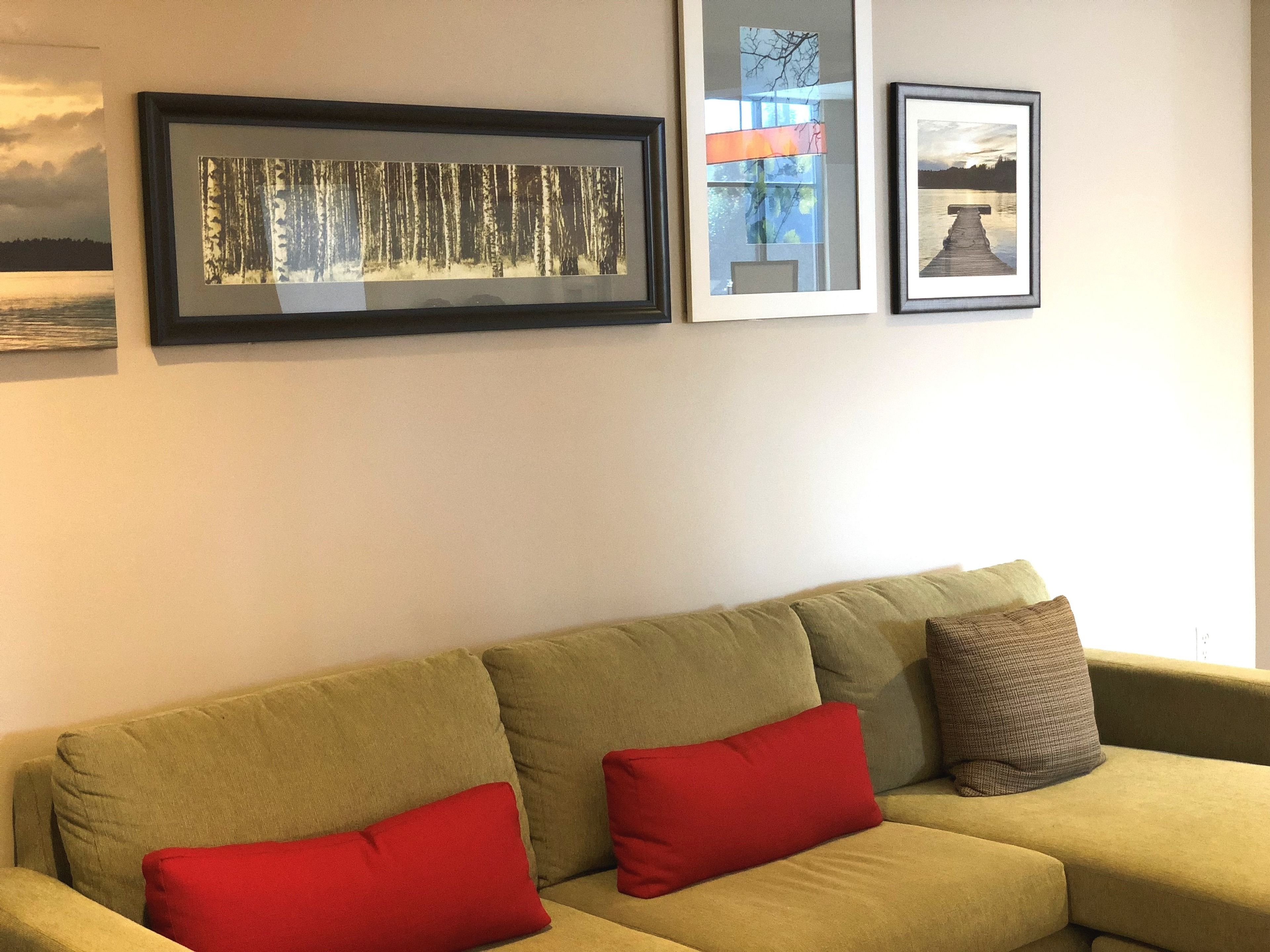 Ein Wohnzimmer mit einem grünen Sofa, zwei roten Kissen und drei gerahmten Bildern an der Wand.