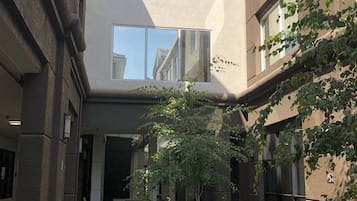 Ein Innenhof mit Außenbestuhlung, ein Gebäude mit großen Fenstern und ein Baum, der Schatten spendet.