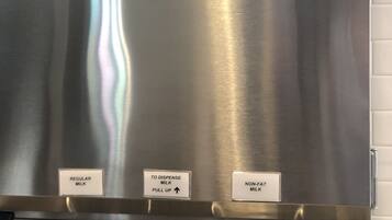 A stainless steel milk dispenser with labels for regular milk, non-fat milk, and a pull-up dispenser.