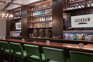A bar area with multiple shelves of liquor bottles, a sign reading 'JACKDAW', and green upholstered bar stools. - DoubleTree by Hilton Denver - Aurora (Aurora)
