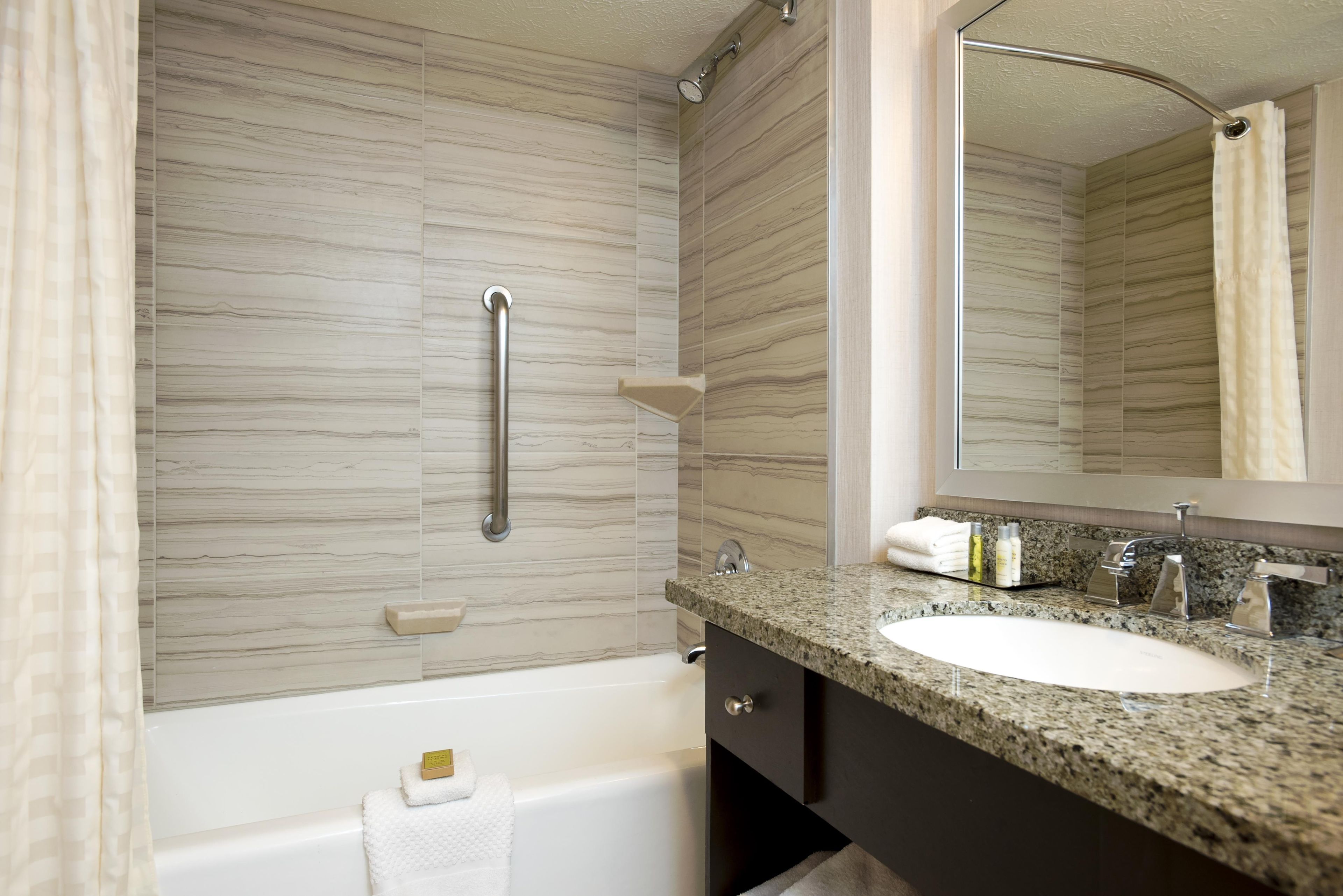 Une salle de bain équipée d’une baignoire, d’un lavabo, d’un miroir et d’une barre d’appui.