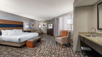 A hotel room with a large bed, a desk, a chair, a vanity with a sink, and a patterned carpet.