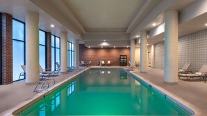 Una piscina interior con agua cristalina, rodeada de sillones de descanso y un muro de ladrillo al fondo.