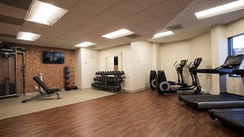A gym with treadmills, elliptical machines, a bench press, and a rack of dumbbells.