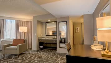A hotel room with a bed, a desk, a chair, a bathroom with a mirror, and a window with curtains.