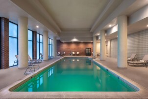 Una piscina interior con agua cristalina, rodeada de sillones de descanso y un muro de ladrillo.