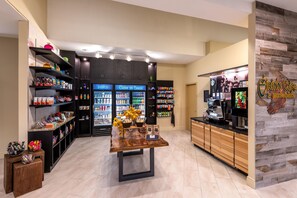 A modern interior with a central table, shelves stocked with snacks, and a coffee machine.